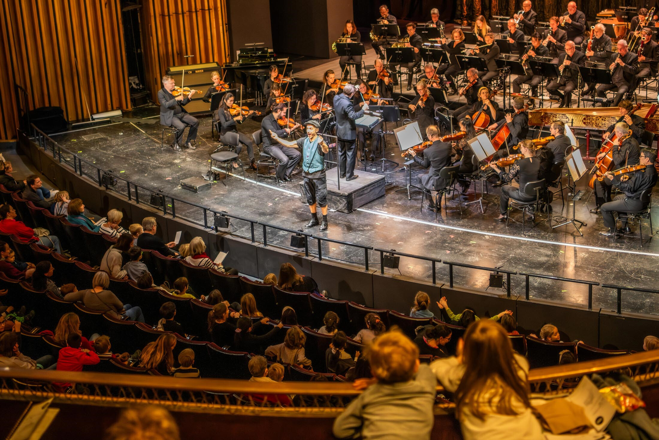 Ein Mann auf einer Bühne, hinter ihm ein Orchester, vor der Bühne im Publikum viele Kinder
