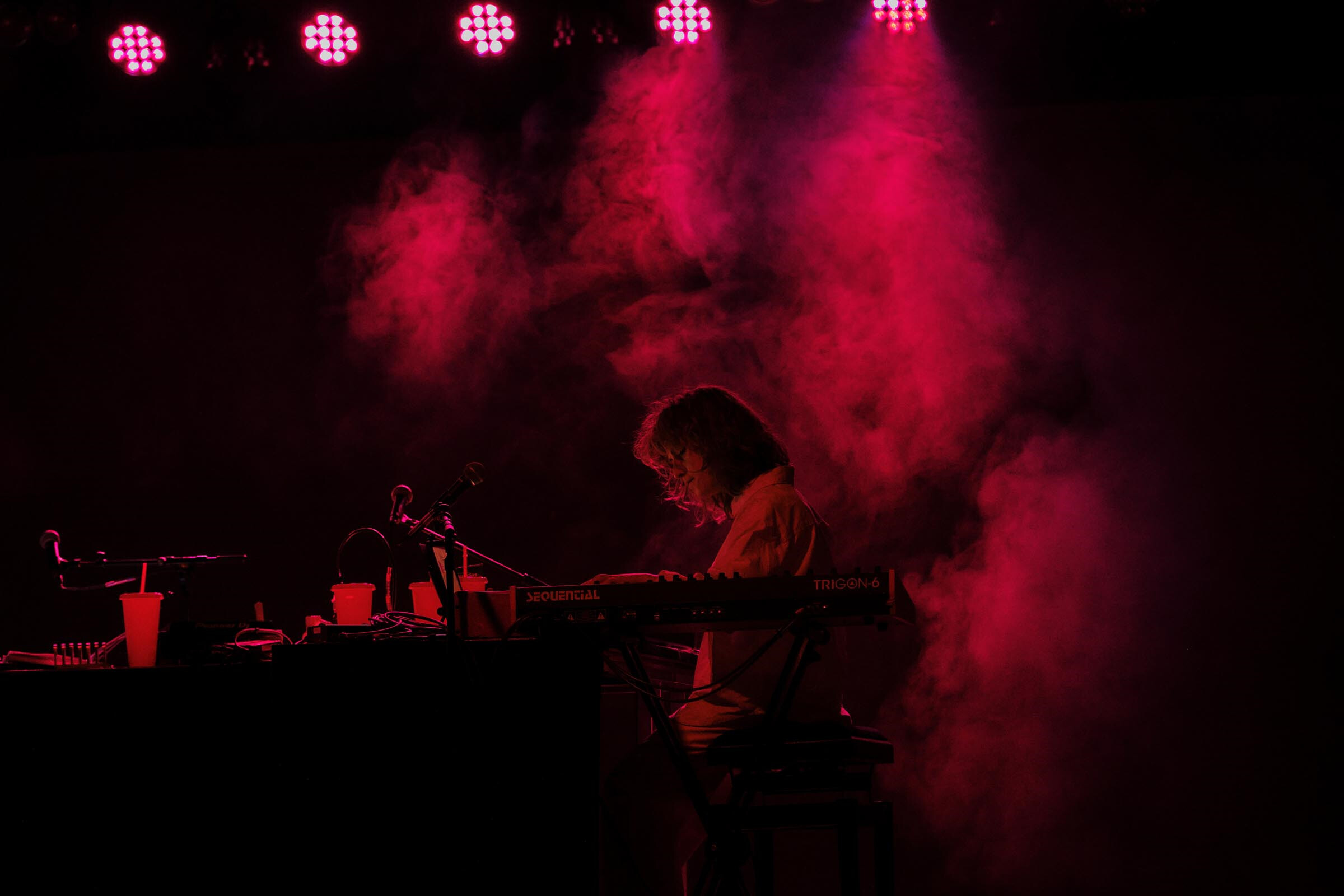 Musikerin spielt verträumt auf Keyboard in rotem Bühnenlicht und Kunstnebel