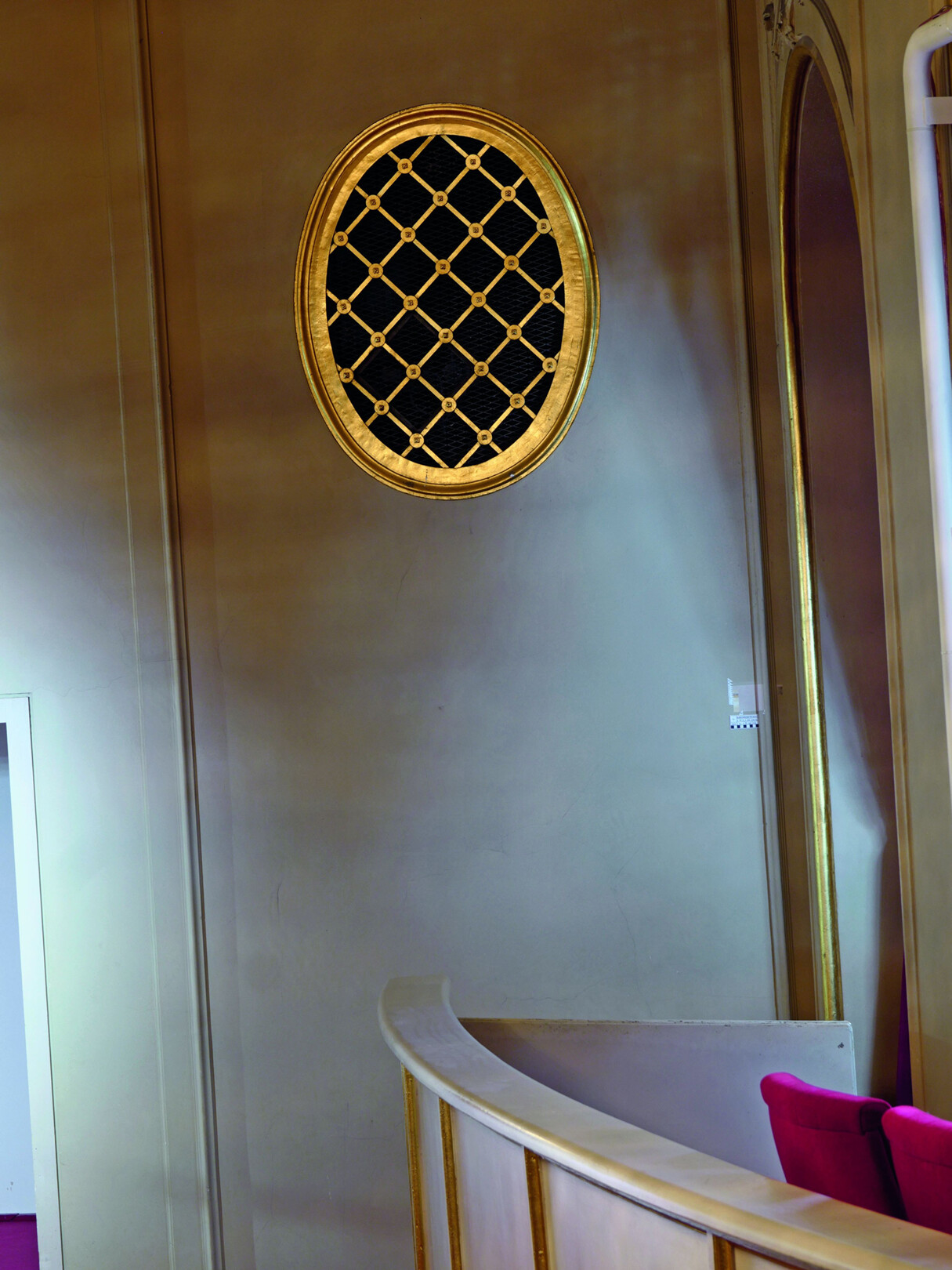 Blick auf helle Wand mit goldenem Lüftungsgitter